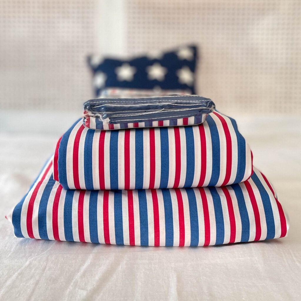 Front view of Ralph Lauren Home American Summer Stripe King sheet set with flat sheet and pillowcases folded and stacked showing red white and blue stripes