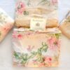 Alternate top-down view of the vintage Ralph Lauren Therese bedding set with folded sheets and pillowcases arranged neatly around a Ralph Lauren placard on cream cotton with pink and sage floral print
