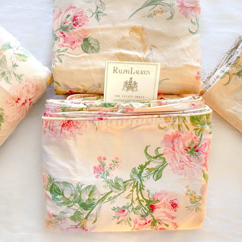 Alternate top-down view of the vintage Ralph Lauren Therese bedding set with folded sheets and pillowcases arranged neatly around a Ralph Lauren placard on cream cotton with pink and sage floral print