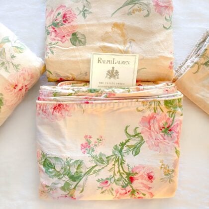 Alternate top-down view of the vintage Ralph Lauren Therese bedding set with folded sheets and pillowcases arranged neatly around a Ralph Lauren placard on cream cotton with pink and sage floral print
