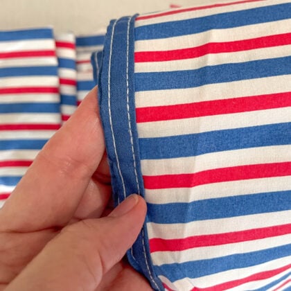 Top down closeup of blue piping on edge of Ralph Lauren American Summer Stripe top sheet showing detailed stitching and striped cotton fabric