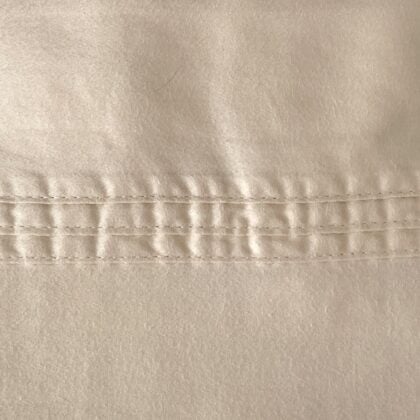 Top-down close-up of the cream king sateen flat sheet showing the three parallel top-stitch rows along the header as a subtle design feature.