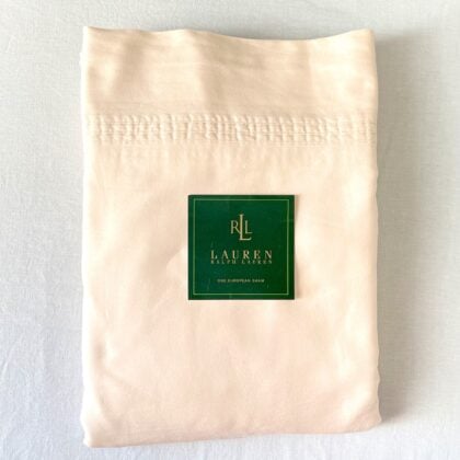 Top-down view of a neatly folded cream king sateen sheet set with the brand placard placed on top, showing its soft sheen and quality.