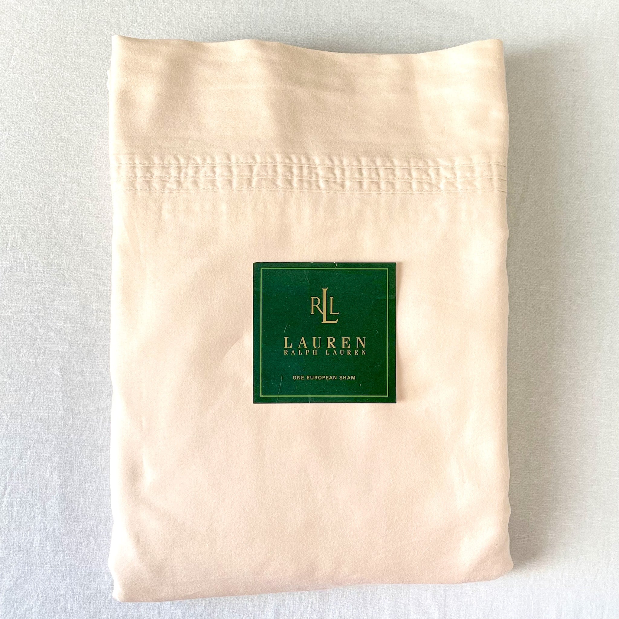 Top-down view of a neatly folded cream king sateen sheet set with the brand placard placed on top, showing its soft sheen and quality.