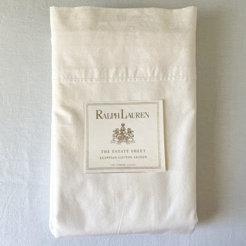 Top-down photo of a neatly folded Polo Ralph Lauren Estate king flat sheet with the white collection placard resting on top.