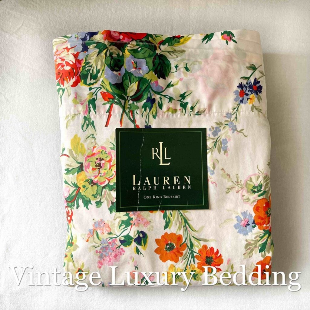 Top-down shot of the Ralph Lauren Belle Harbor king flat sheet neatly folded with the Ralph Lauren placard, featuring colorful pink and red peonies and multicolor wildflowers on a soft white background.