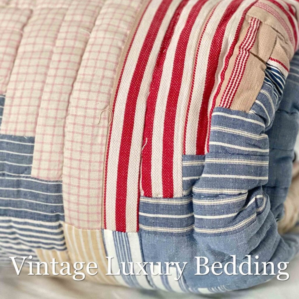 Close-up side shot of the folded and rolled Ralph Lauren Chadwick Blue King Patchwork Quilt showing soft red, white, light blue, and cream patchwork strips