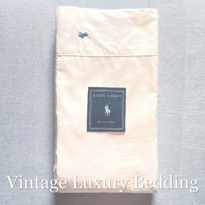 Top-down photo of the off-white Polo Ralph Lauren Estate king sateen flat sheet showing the embroidered Polo horse logo and the blue Ralph Lauren placard.