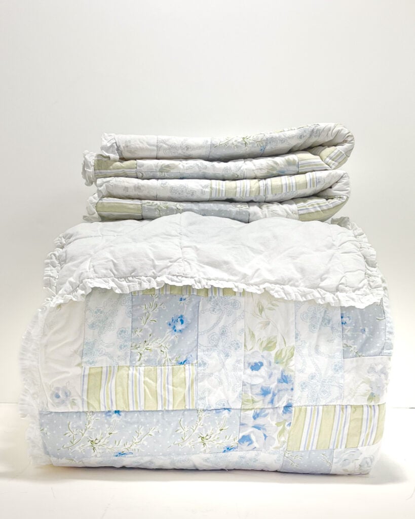 Simply Shabby Chic British Rose king patchwork quilt folded with matching white ruffled pillow shams in soft blue, white, and pale green floral patchwork