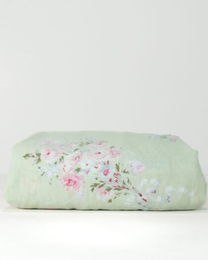 Side view of a neatly folded Simply Shabby Chic Ribbons and Roses Bouquet 60 by 80 inch tablecloth with sage background and pink rose bouquets