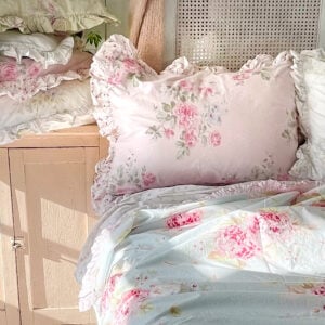 Styled Simply Shabby Chic bed with Peony Rose ruffled sham, Hydrangea Blue duvet, and British Rose ruffled shams in morning sunlight against a caned headboard