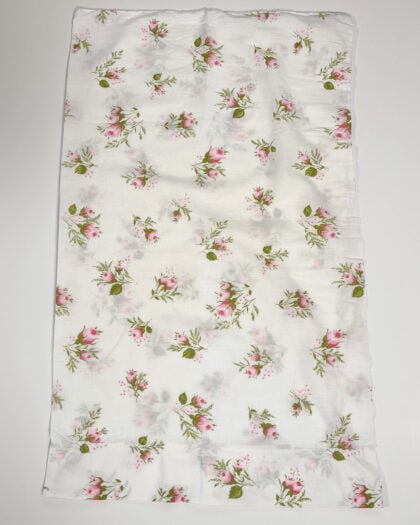 Full flat lay of vintage white cotton pillowcase with scattered pink rosebud floral pattern
