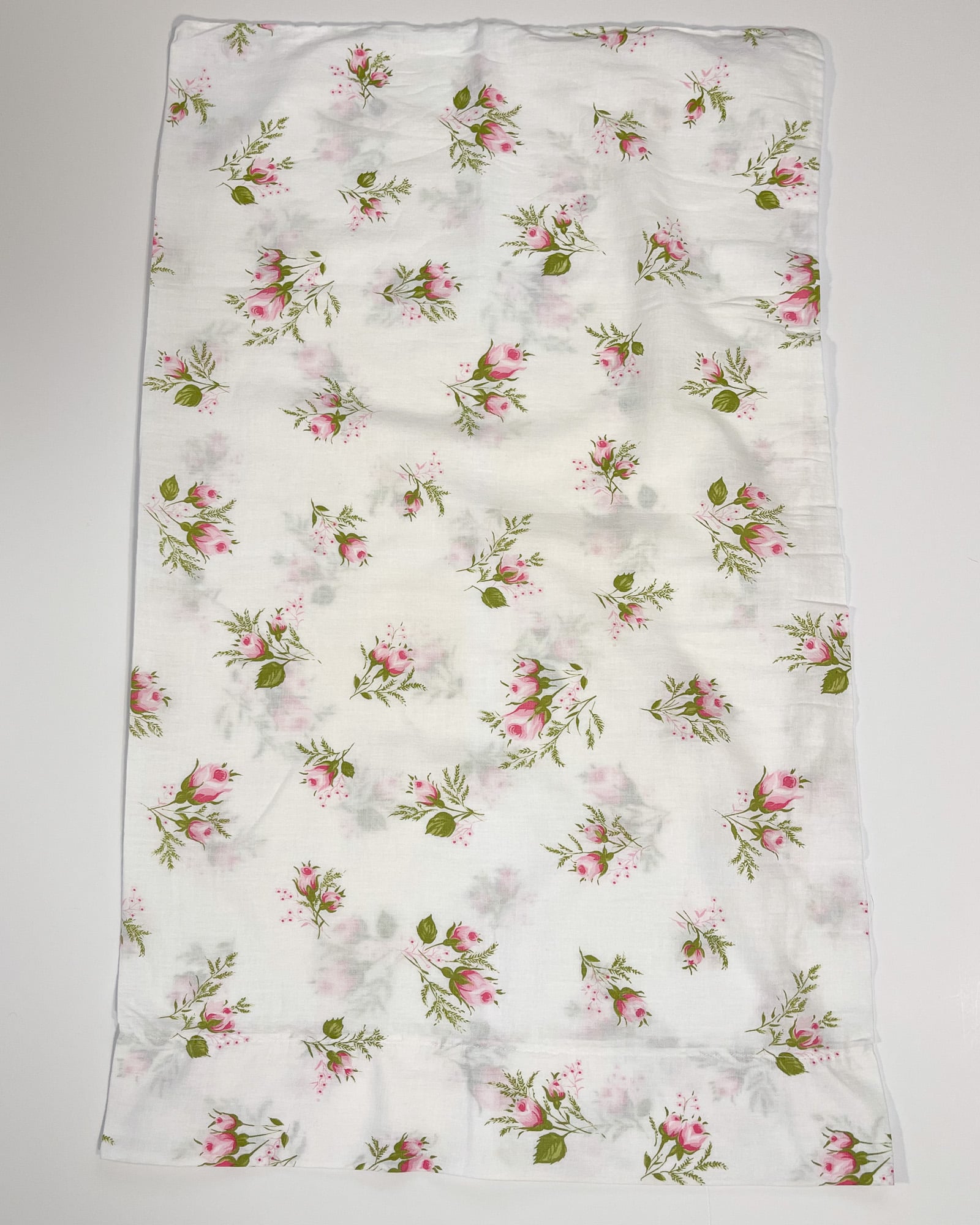 Full flat lay of vintage white cotton pillowcase with scattered pink rosebud floral pattern