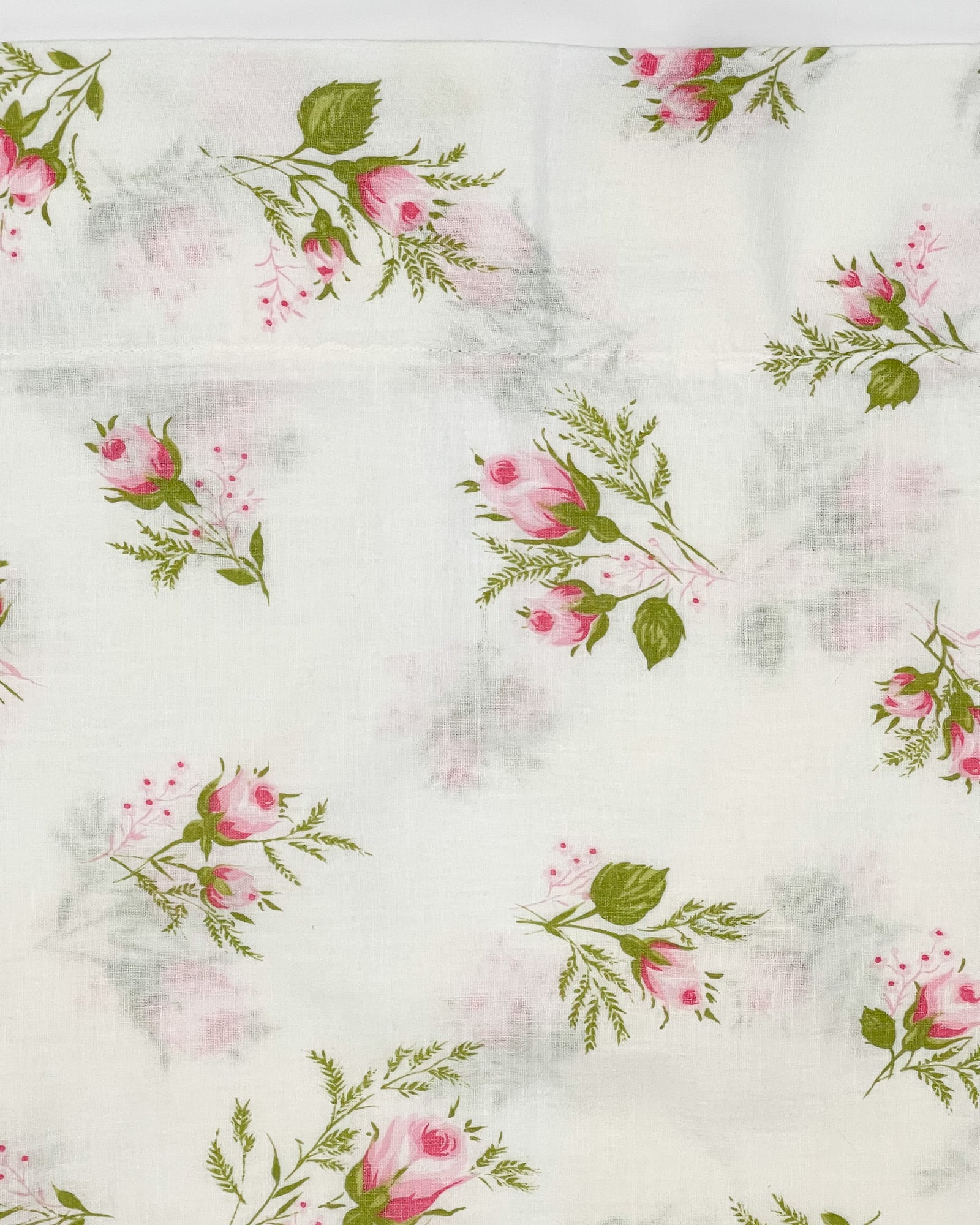 Medium close-up of pink rosebud floral print with green foliage on white cotton pillowcase